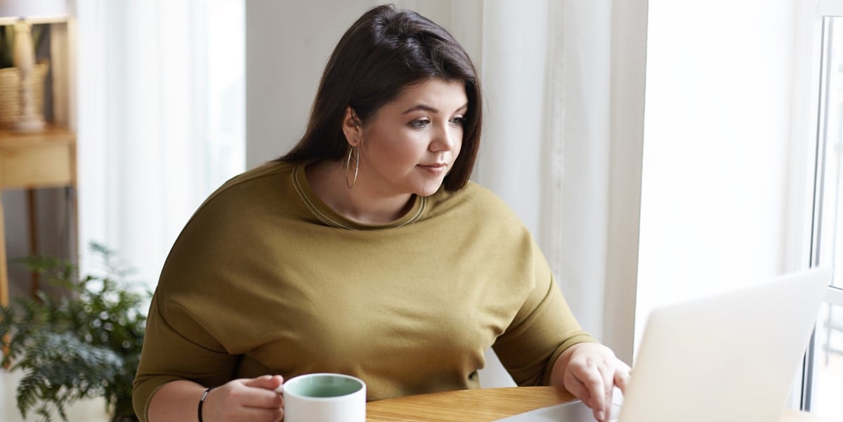 professional woman in office with laptop, holding coffee cup