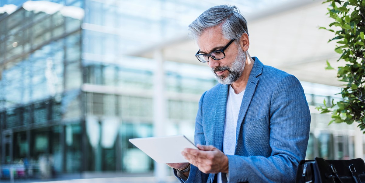 professional man sitting outside office building reading tablet