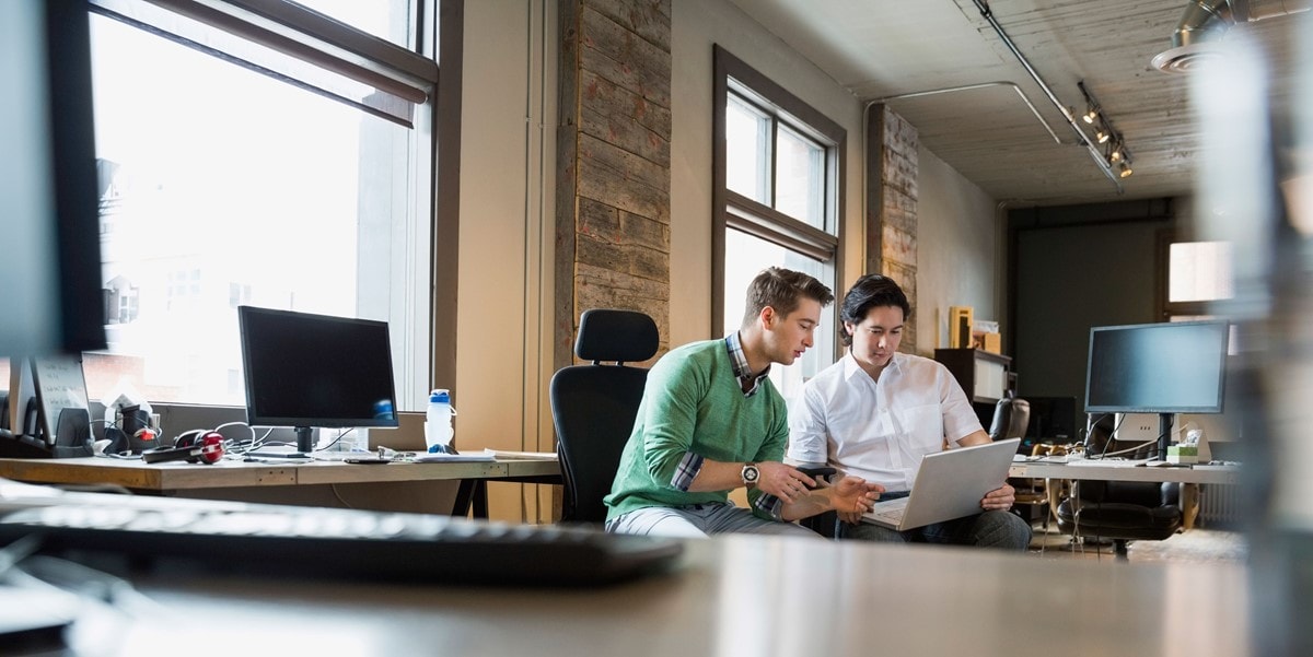 two men collaborating on work over a laptop