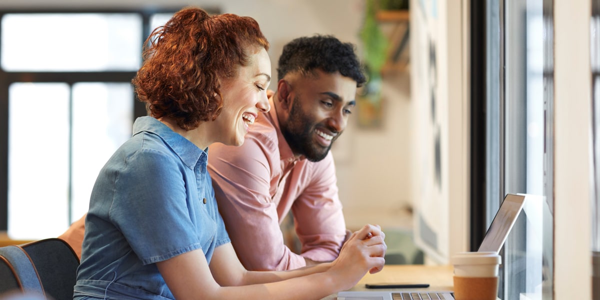 Mujer y hombre sentados, sonriendo mientras ven la pantalla de so computadora personal