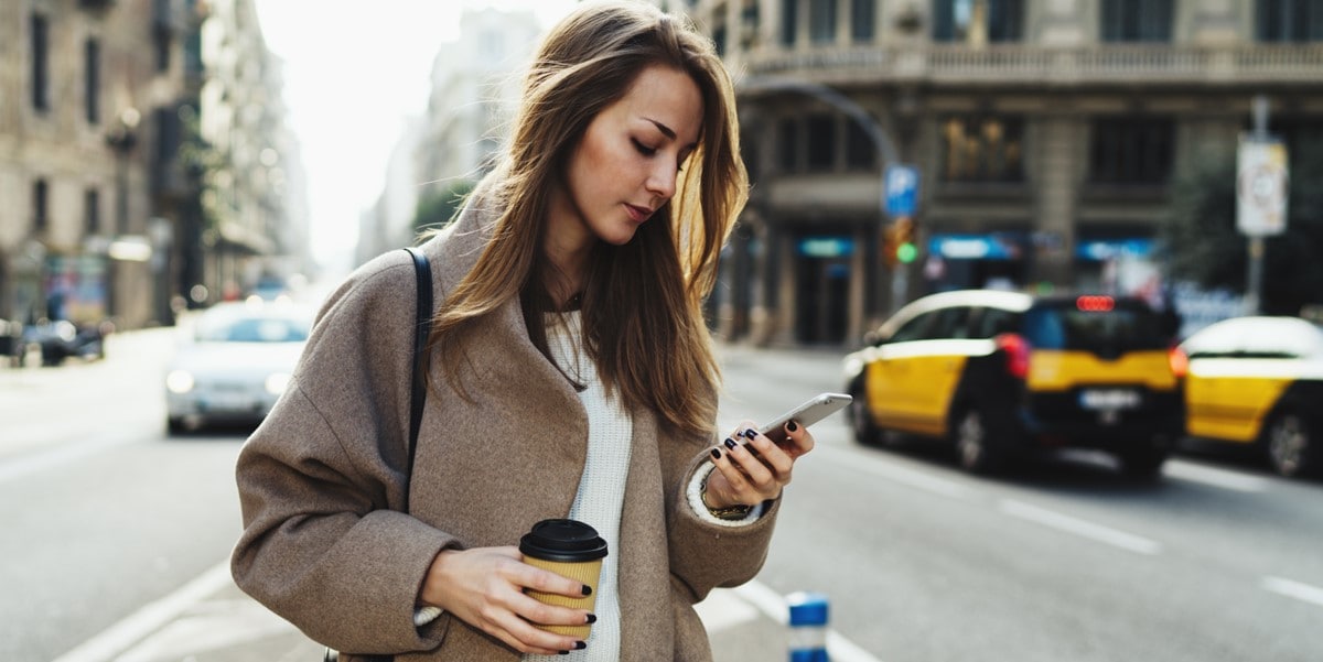mujer parada afuera, ciudad, viendo celular
