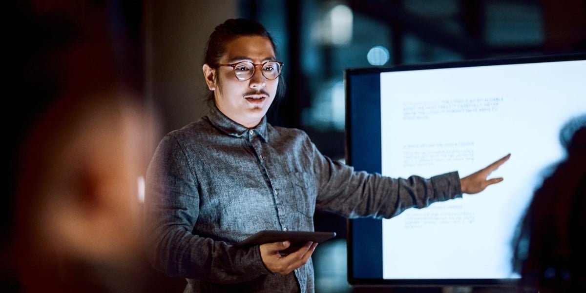 professional man in office giving a presentation, gesturing to screen
