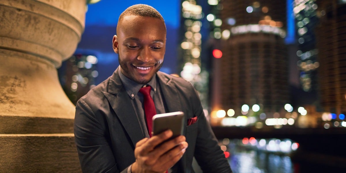 businessman sitting outside looking at cell phone, city buildings in the backgrounnd