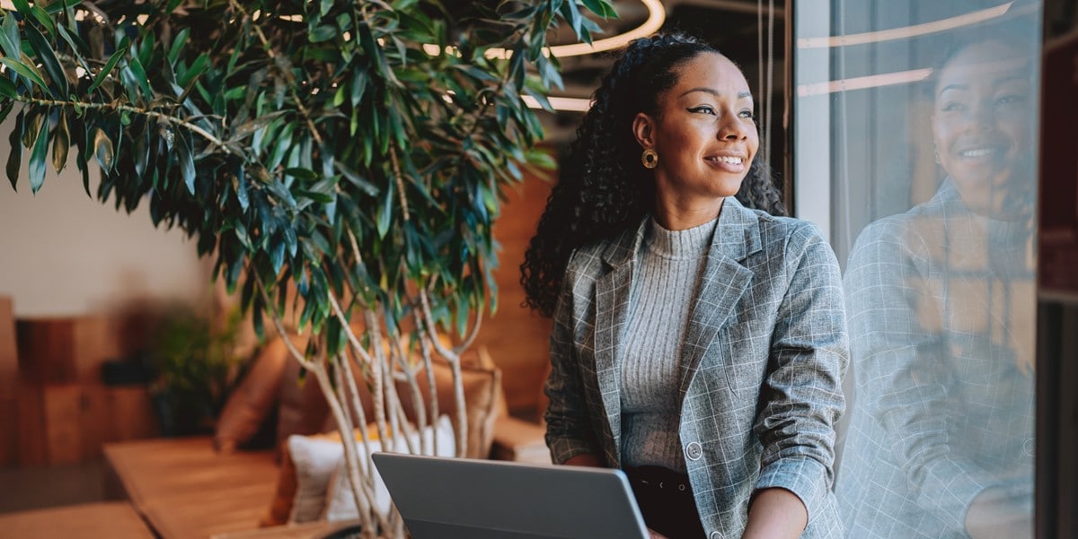professional woman smiling, in the office, looking out window, with laptop